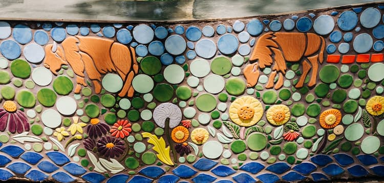 A mosaic panel of two buffalo grazing on rolling green hills, sunflowers sprouting in the grass, above blue tiles representing Beargrass Creek